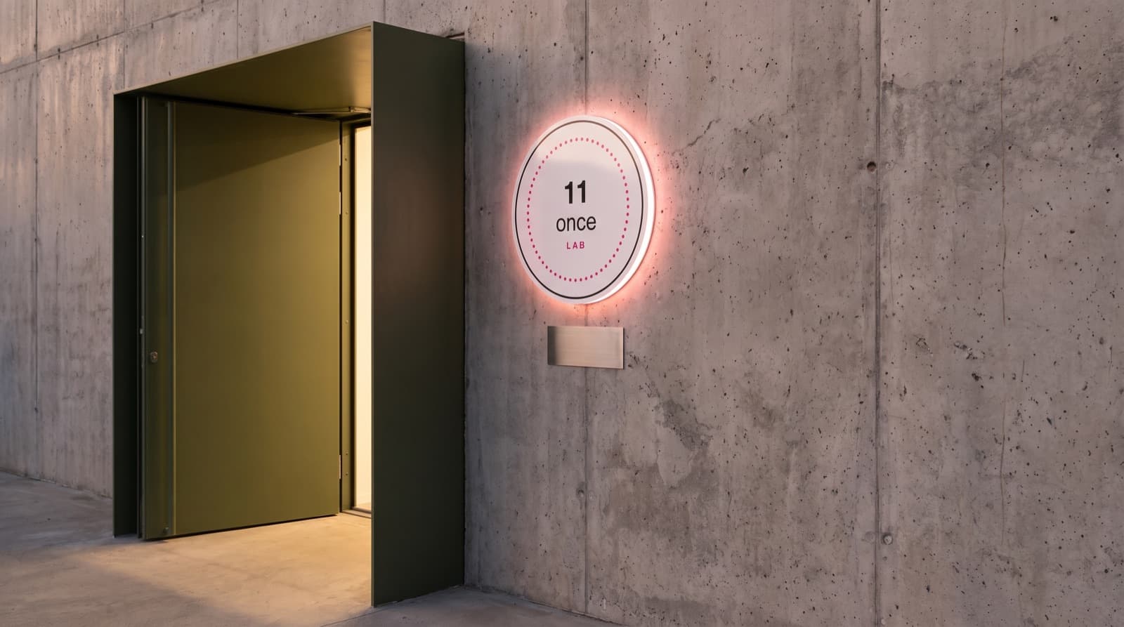Sello circular retroiluminado con halo rosa, montado en un muro de concreto junto a una puerta.